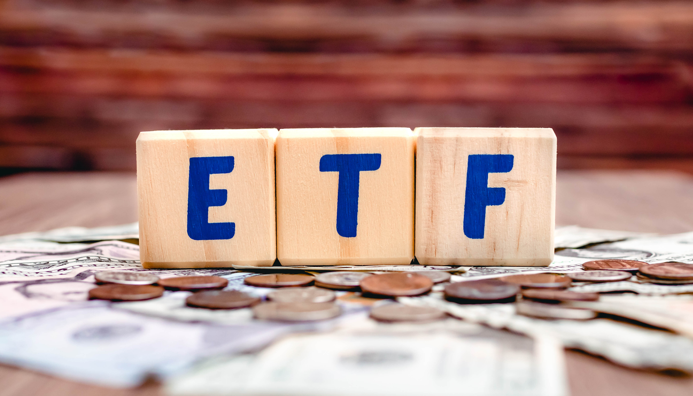 Wooden cubes with blue letters forming the word ETF (Exchange Traded Funds) on dollar bills on a table. Investment concept photo.